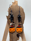 Orange jack-o’-lantern witch hat earrings with black faceted beads hanging on a wooden display